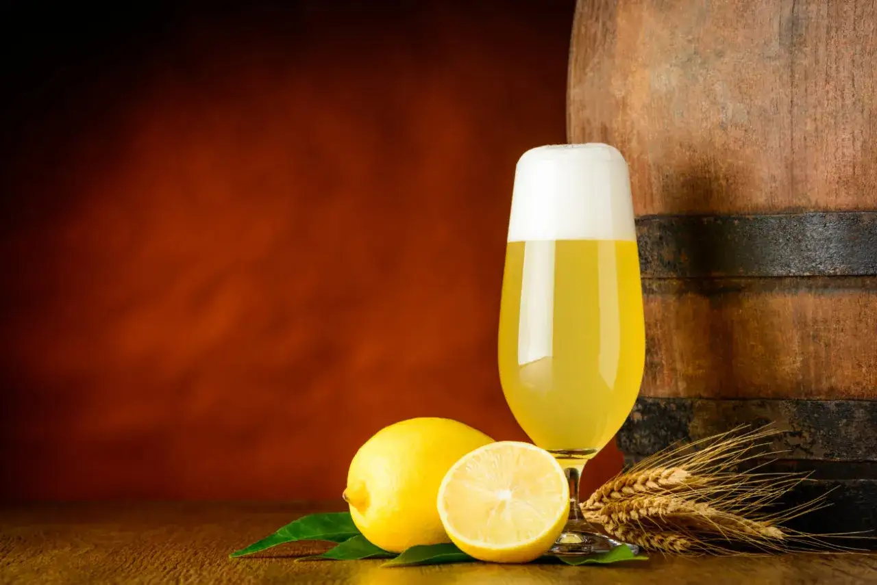 Ein Glas Radler mit Zitronen und Gersten&auml;hren neben einem Holzfass. Perfekt zum Radler mischen!