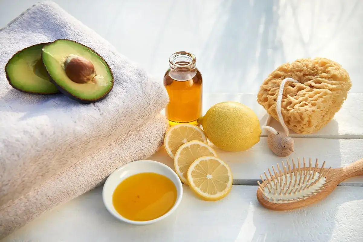 Zutaten für eine natürliche Avocado-Haarmaske: Avocado, Zitrone, Honig und Öl. Dazu ein Schwamm und eine Bürste.