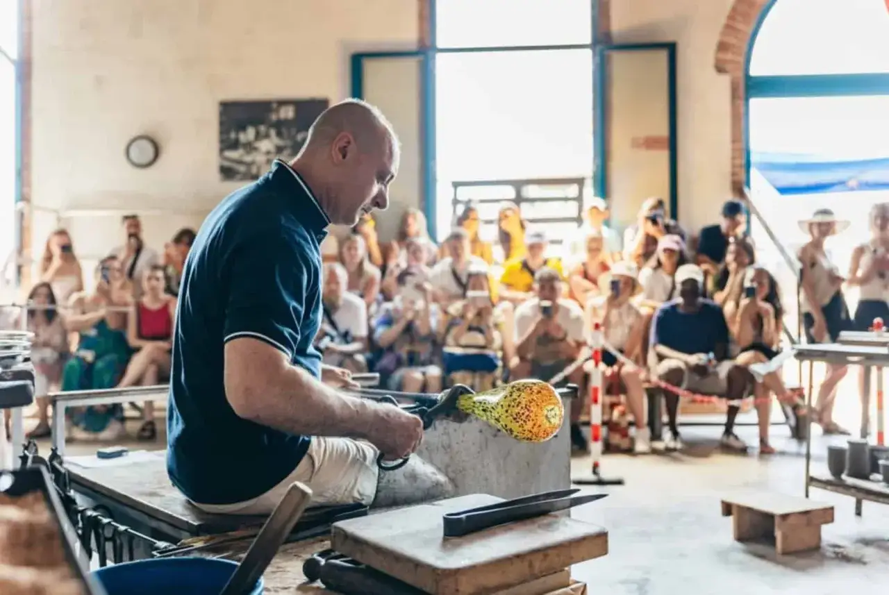 Artisan verrier à Murano Venise, façonnant une pièce de verre colorée devant un public captivé.