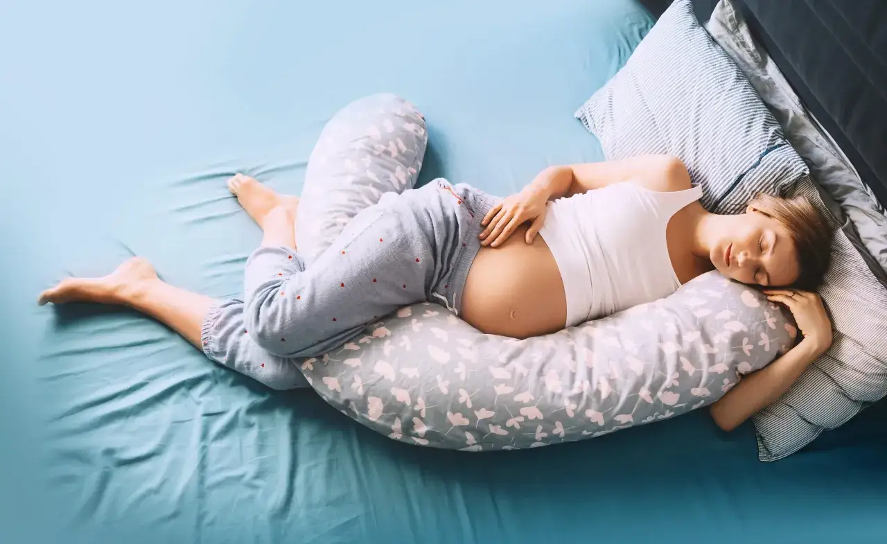 Donna incinta dorme serena sul fianco, supportata da un cuscino da gravidanza. Un'immagine che mostra come dormire in gravidanza in modo confortevole.