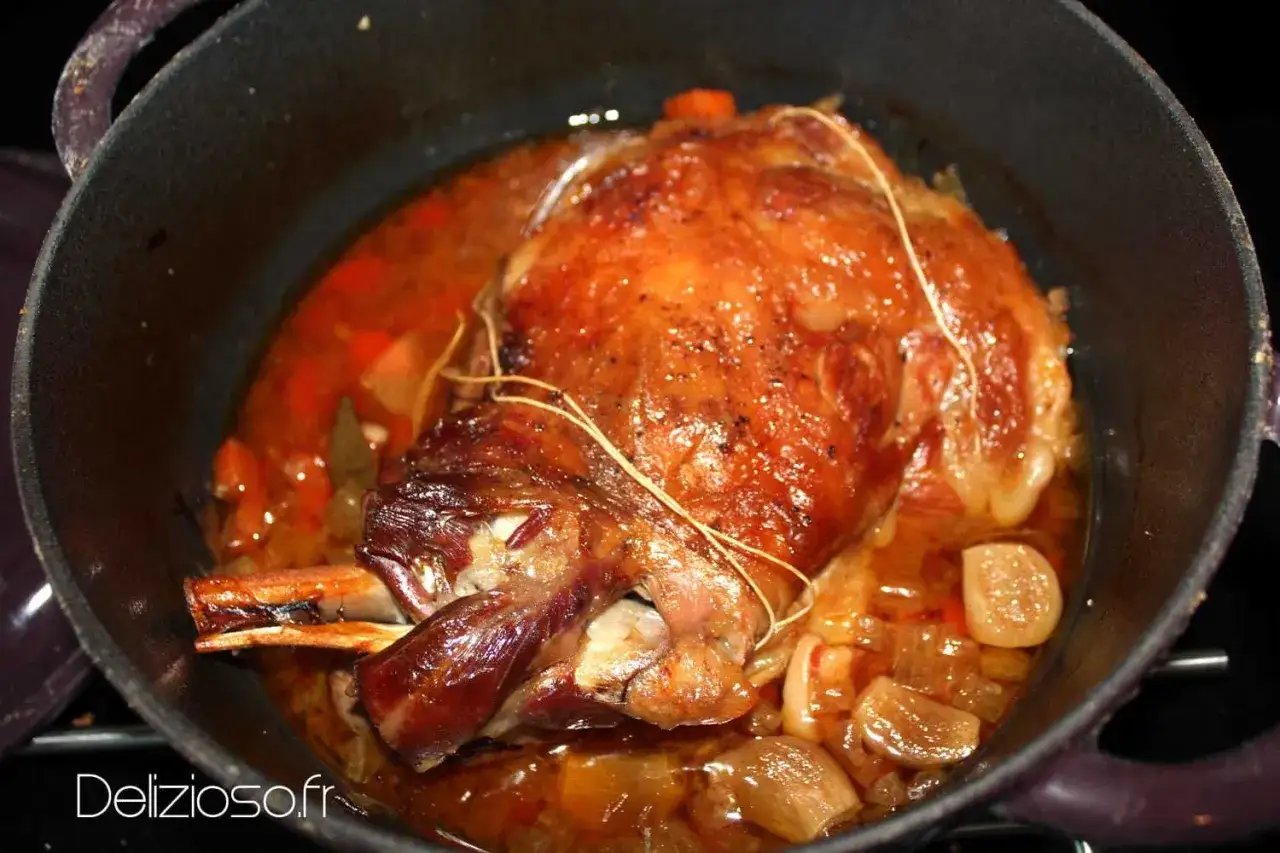 Une succulente épaule d'agneau rôtie dans sa cocotte, baignant dans un jus savoureux avec des oignons et des carottes.