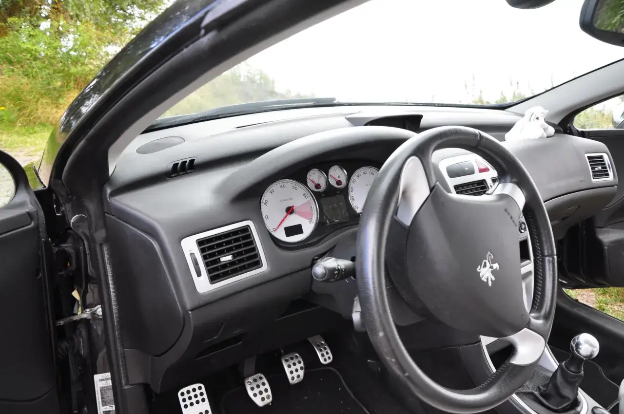 Interiör av en Peugeot 307 CC. En liten vit fårfigur sitter på instrumentbrädan, kanske en ledtråd till ett Peugeot 307 CC problem?