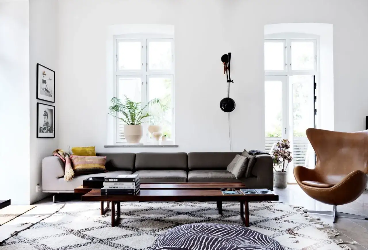 Ett modernt vardagsrum med en mörkgrå soffa, en brun läderfåtölj och en låg träsoffa. Mönstrat överkast och kuddar ger färg. Här finns många måla ideer för inredning.