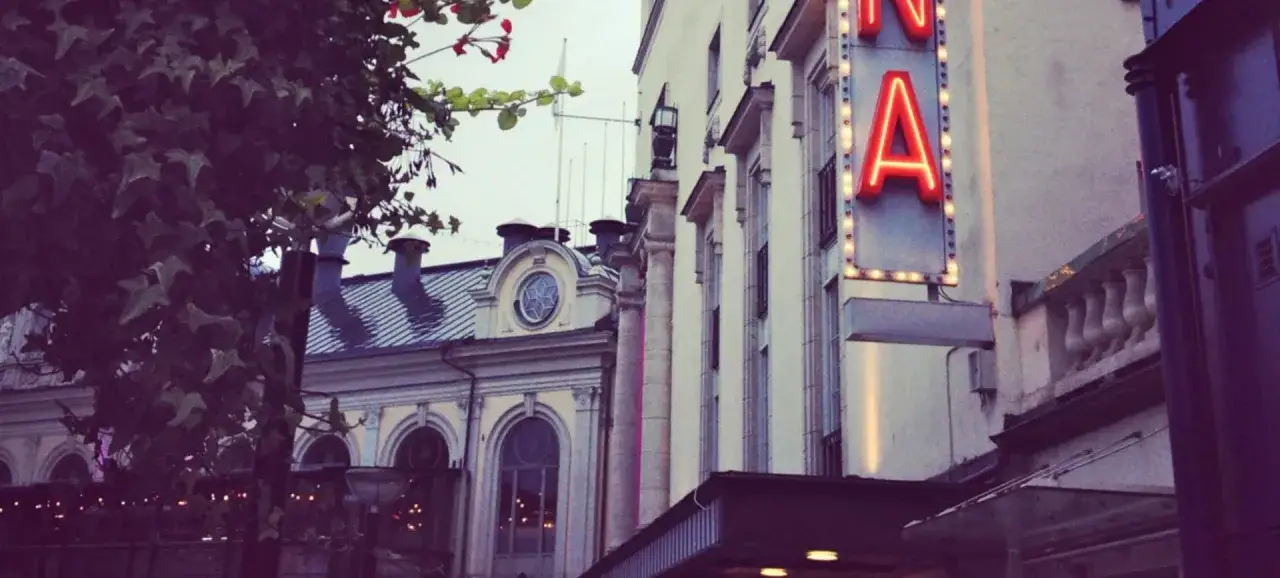 Neonskylt lyser upp fasaden vid China Teatern Stockholm. Tr&auml;d med blommor skymtar till v&auml;nster.