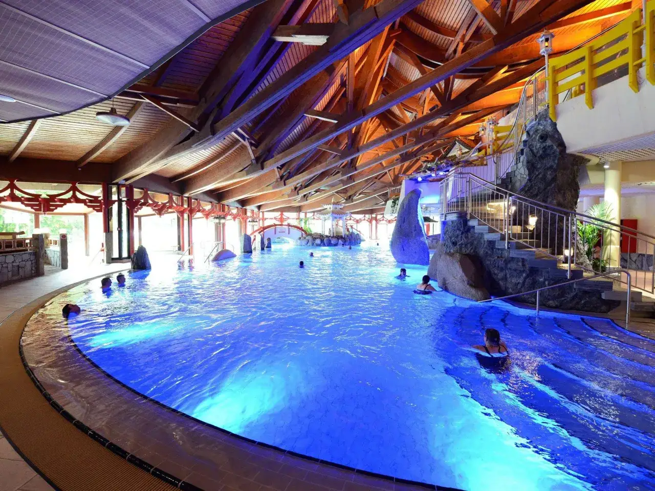 Entspannter Urlaub in Hessen: Ein gro&szlig;es Schwimmbad mit blauer Beleuchtung, Felsen und einer Rutsche.