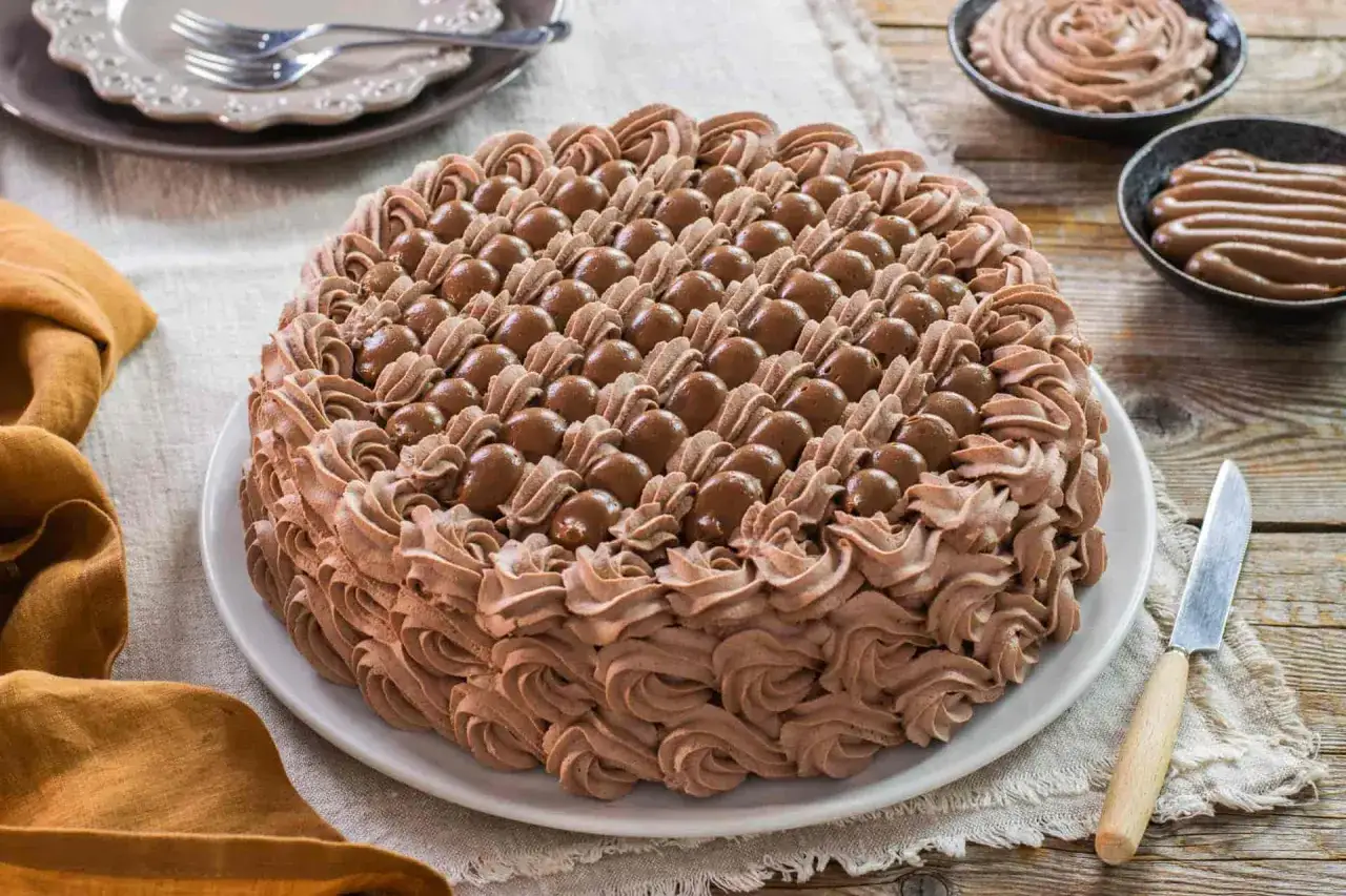 Torta ricoperta da abbondante crema chantilly al cioccolato, decorata con sfere di cioccolato e riccioli di crema.
