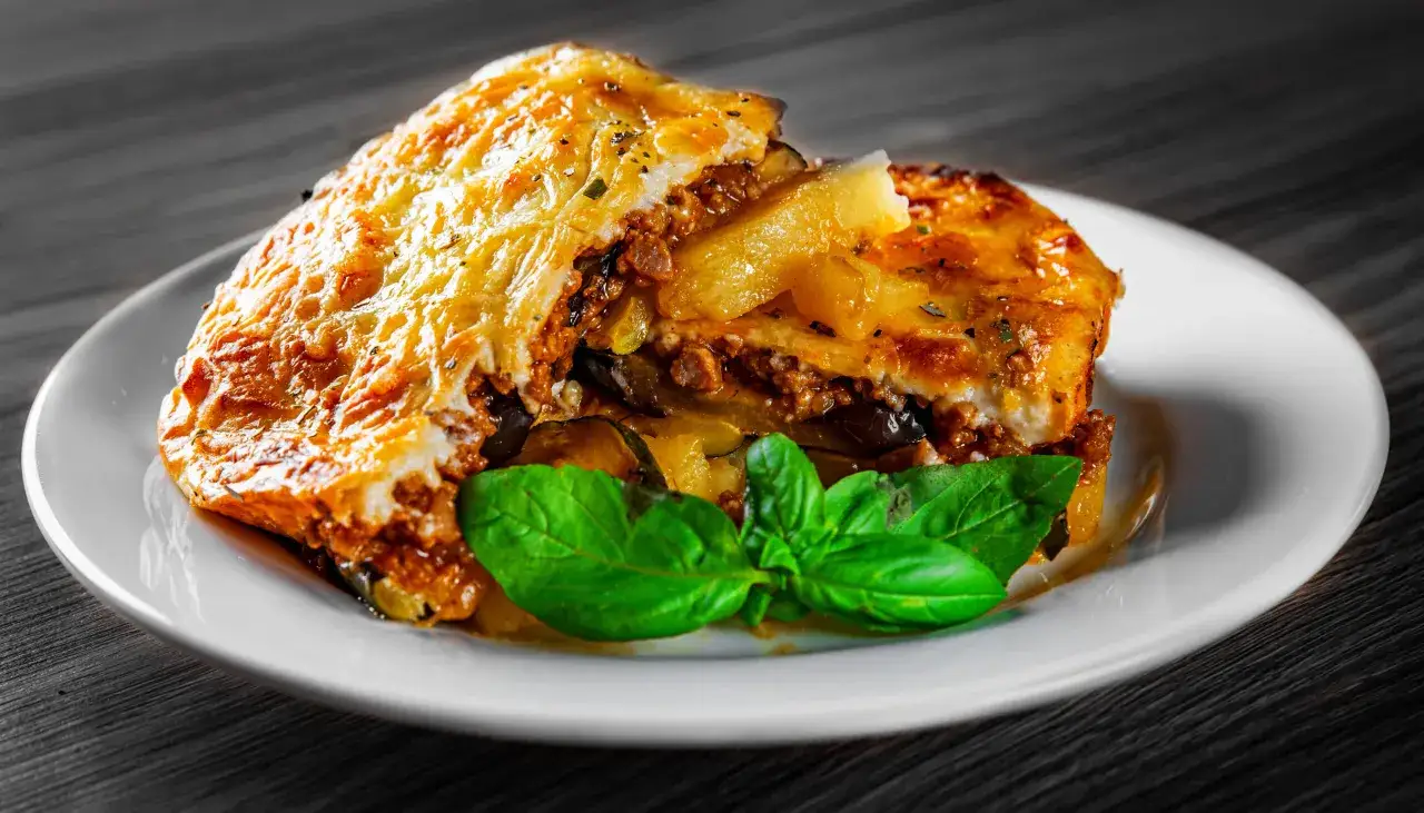 En bit moussaka med potatis och aubergine, toppad med gyllene ost och garnerad med färsk basilika.