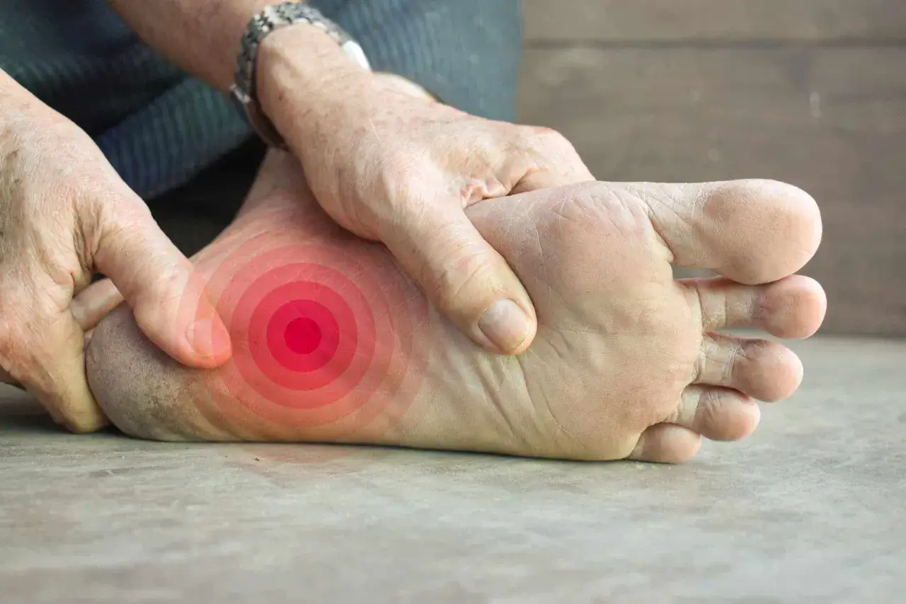 Schmerzende Ferse, die durch rote Kreise hervorgehoben wird. Eine Hand massiert den Bereich, um die Fußschmerzen zu lindern.