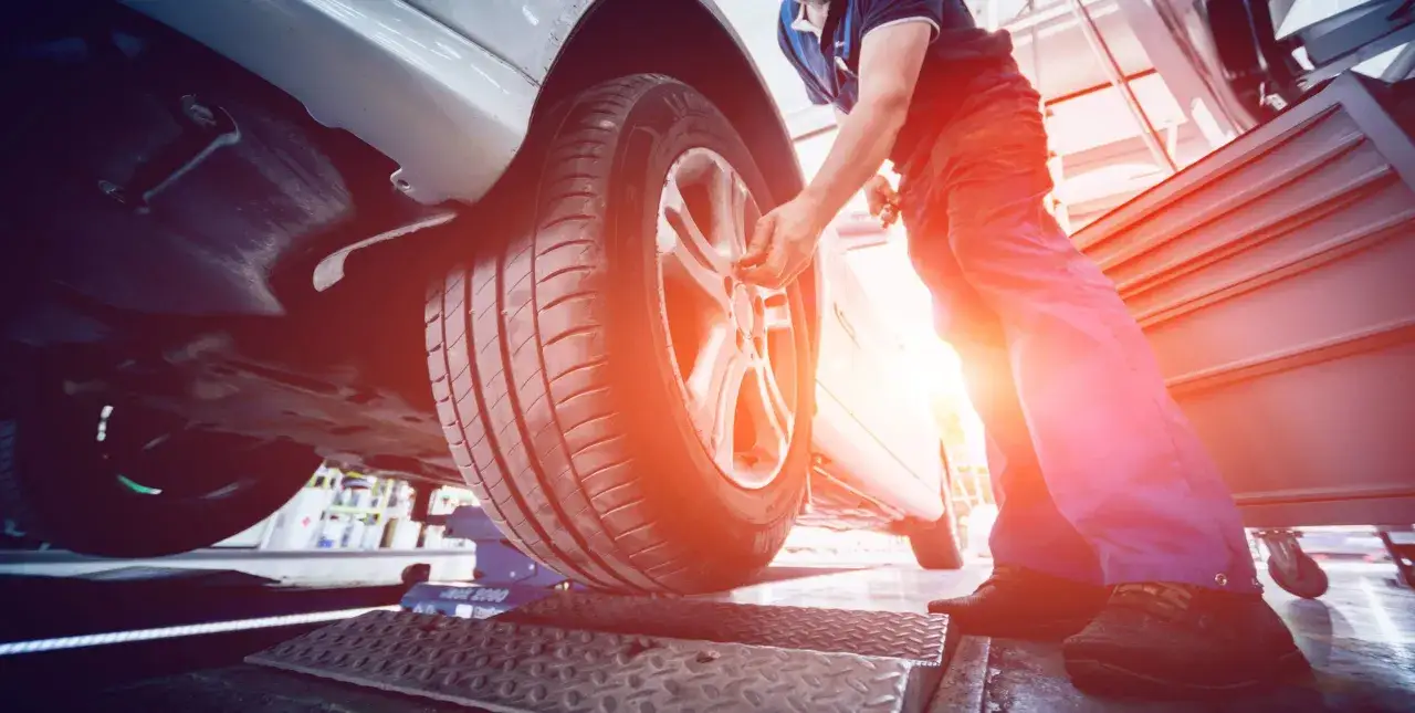 Meccanico effettua la manutenzione pneumatici di un'auto sollevata.