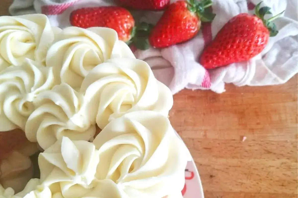 Dolce torta decorata con ciuffi di namelaka al cioccolato bianco, accompagnata da fragole rosse su un canovaccio.