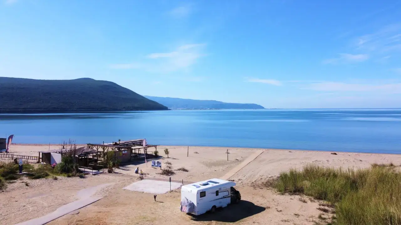 Kamper na piaszczystej plaży, z widokiem na spokojne morze i zielone wzgórza. Idealne miejsce, by odkrywać walory turystyczne Grecji.