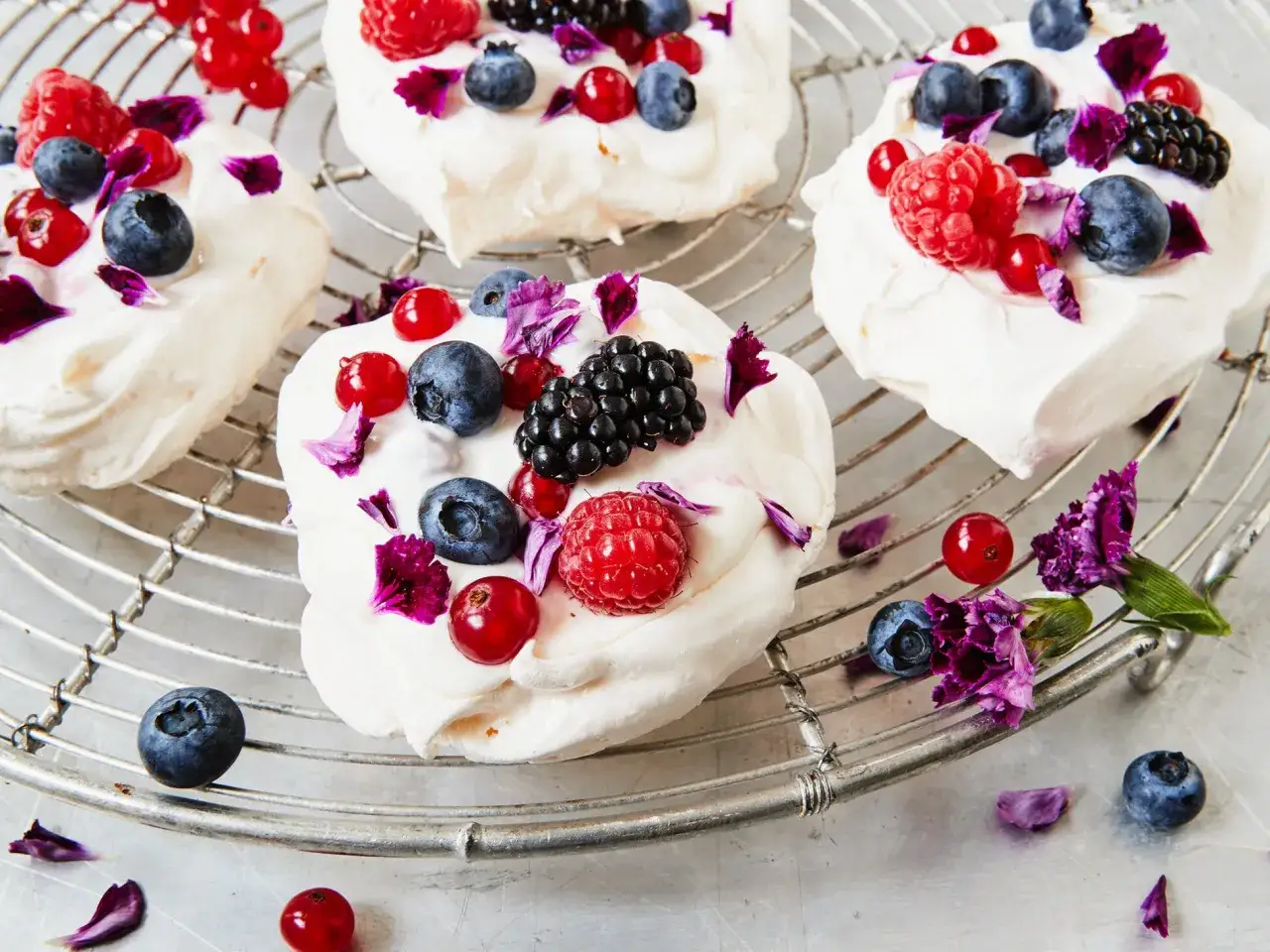Pavlova-Törtchen mit Mascarpone, Beeren und Blütenblättern auf einem Gitter. Ein köstliches Pavlova-Rezept mit Mascarpone.
