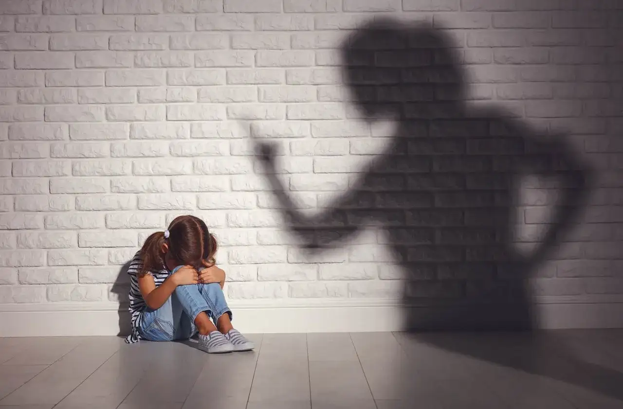 Ein M&auml;dchen kauert weinend auf dem Boden, w&auml;hrend ein bedrohlicher Schatten einer erwachsenen Person an der Wand erscheint. Psychologie: Mutter hasst Tochter?