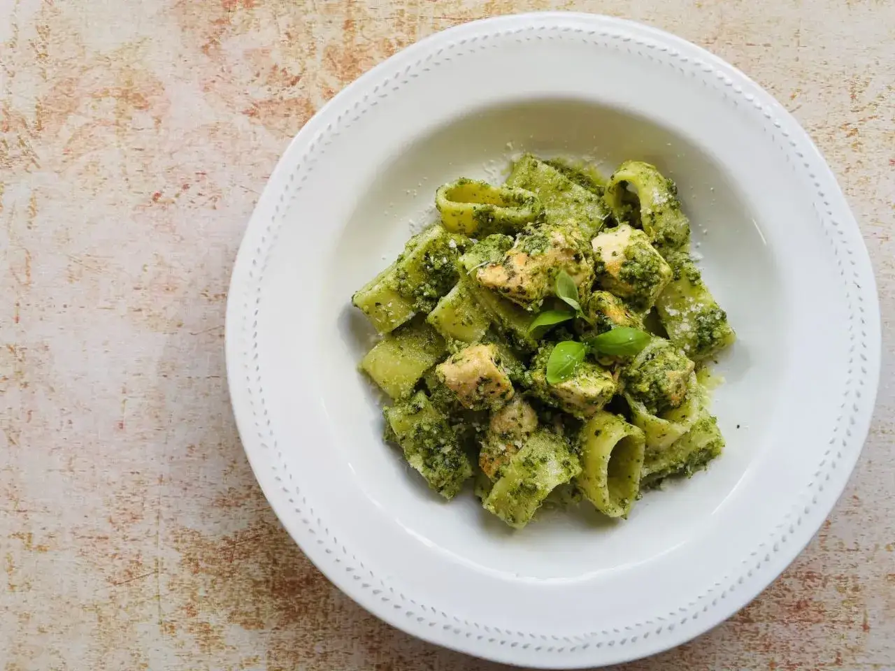 Pyszny makaron z pesto i kawałkami kurczaka, posypany parmezanem. Idealny na szybki obiad.