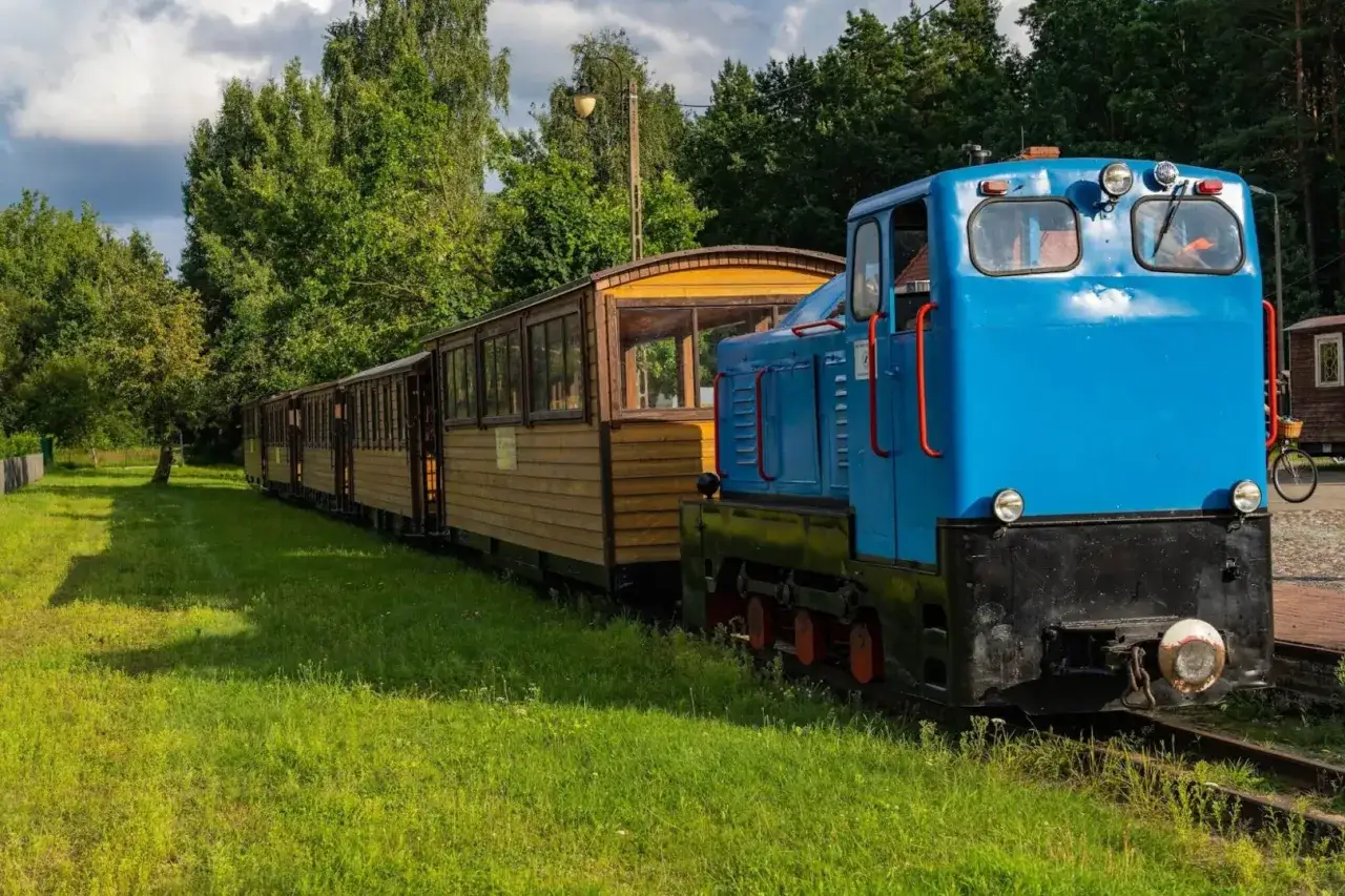 Niebieska lokomotywa i drewniane wagony czekają na pasażer&oacute;w. Idealne **hajn&oacute;wka atrakcje dla dzieci** na letnią przygodę.