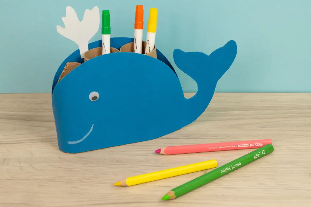 Blauer Wal-Stiftehalter basteln: Ein lustiges DIY-Projekt für Kinder. Bunte Stifte und ein aufgemalter Mund machen den Wal lebendig.