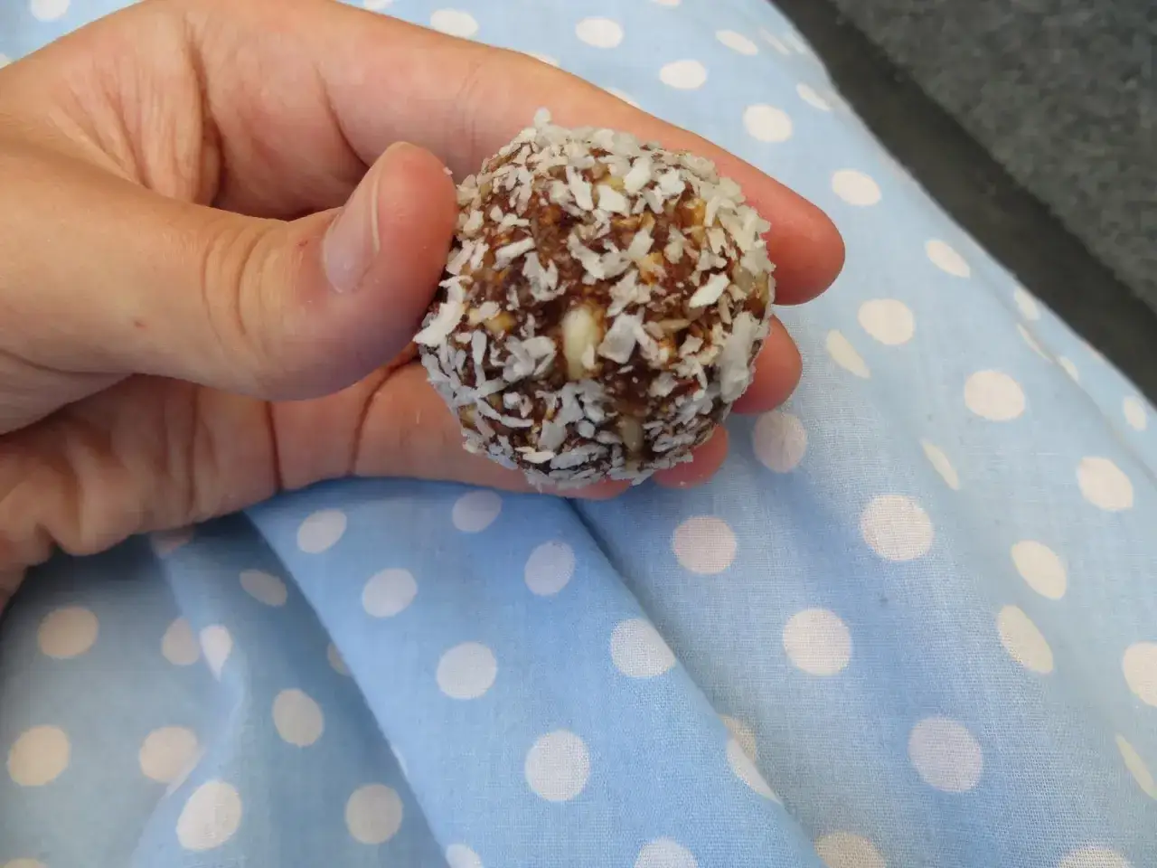 En hand håller en dadelboll täckt med kokosflingor. Ett perfekt resultat av ett enkelt dadelbollar recept.