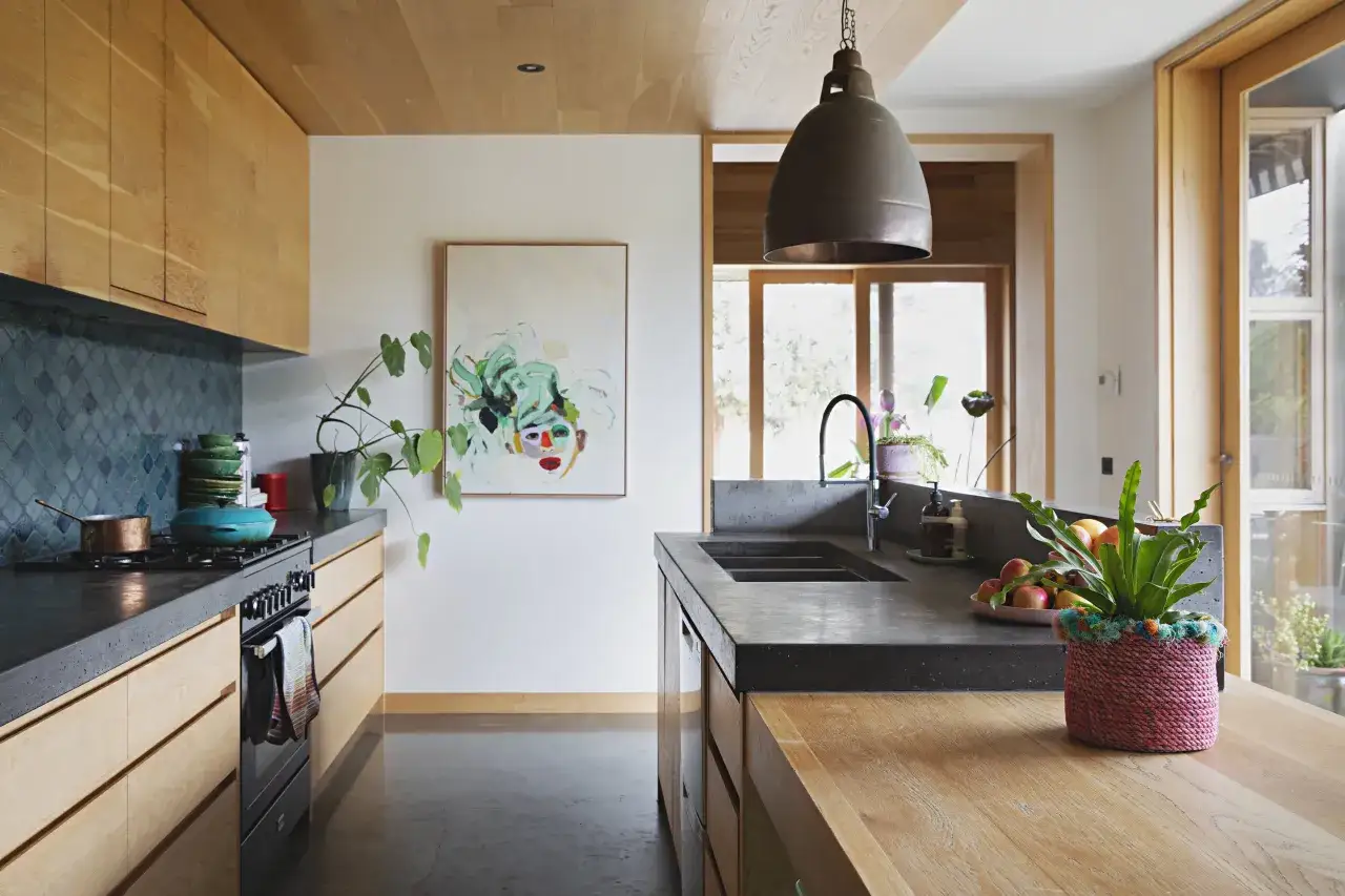 Une cuisine moderne avec un plan de travail en béton, des placards en bois clair et un carrelage bleu profond. La déco du plan de travail cuisine inclut une plante verte et des fruits.