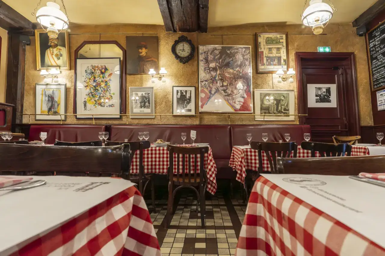 Ambiance chaleureuse d'un bistrot parisien avec tables dressées, banquettes rouges et œuvres d'art aux murs.