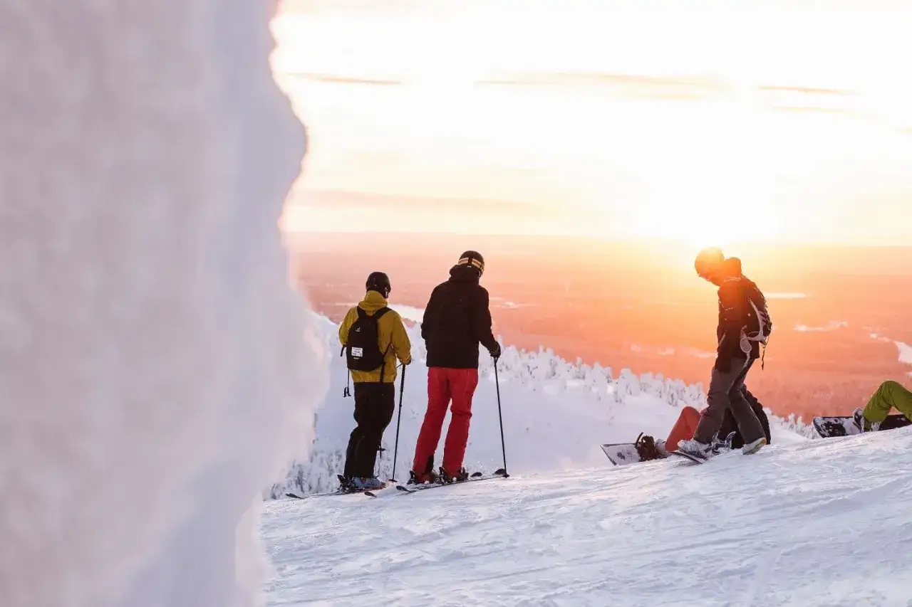 Zachód słońca w Laponii. Narciarze i snowboardziści podziwiają piękną pogodę i krajobraz.
