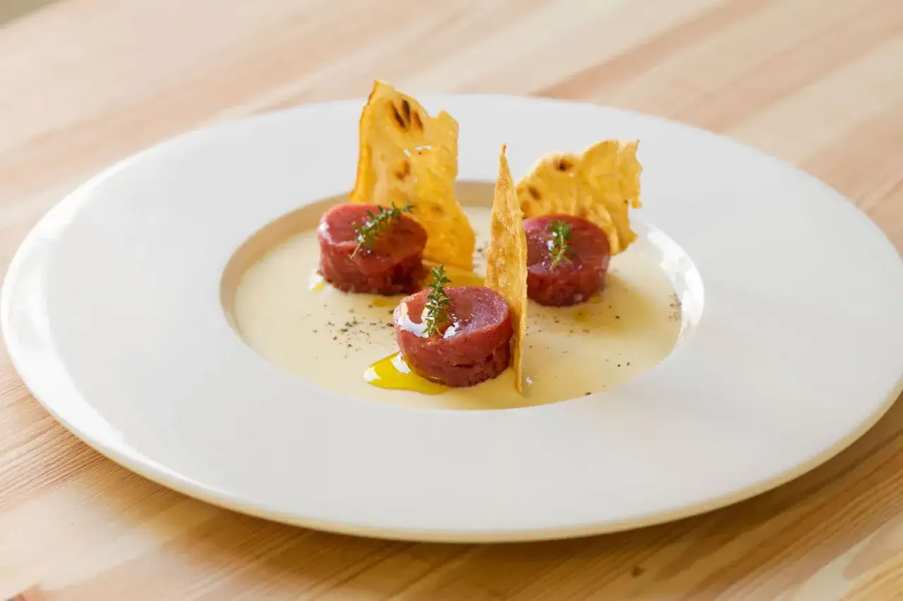 Tre porzioni di tartare di manzo, guarnite con timo e accompagnate da croccanti cialde, su una crema chiara.