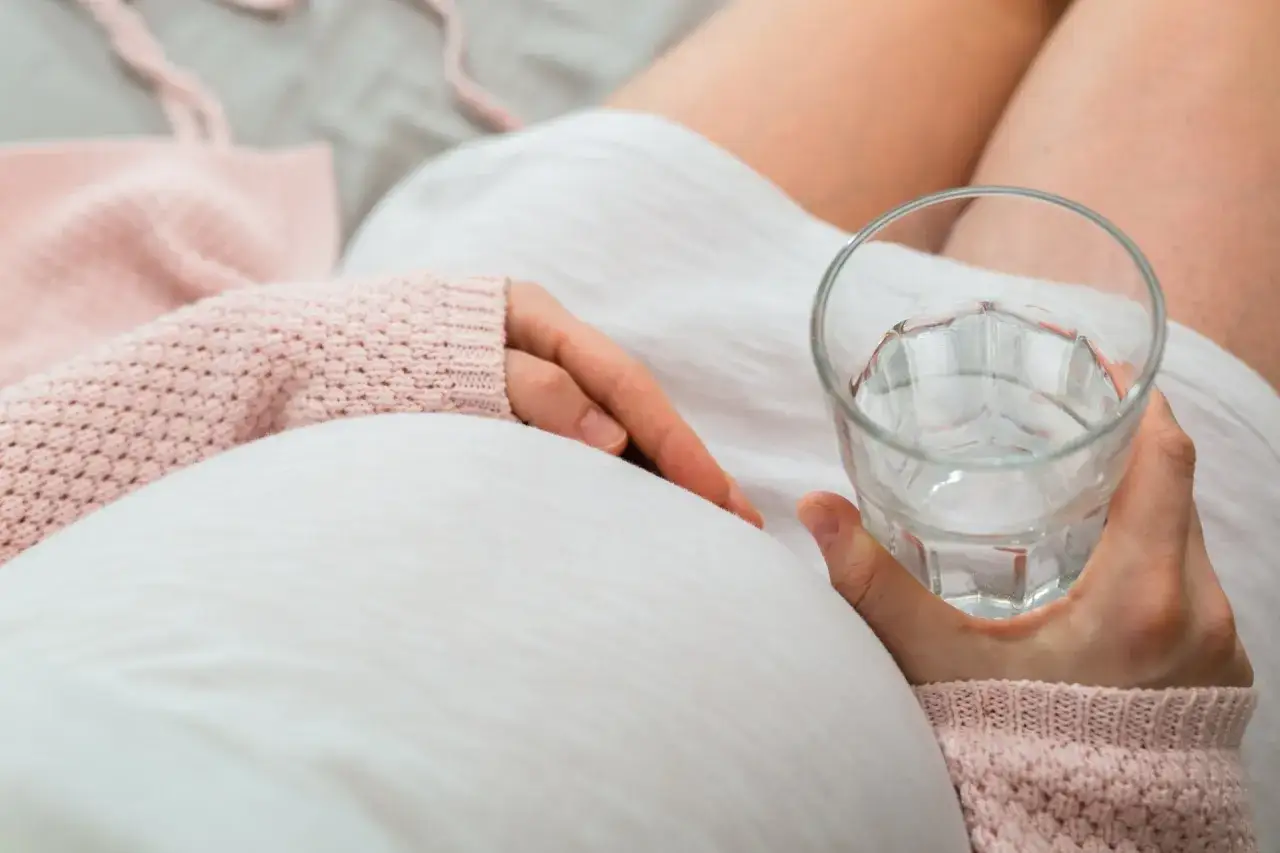 Kobieta w ciąży trzyma szklankę wody, dbając o komfort. Laktuloza w ciąży może pom&oacute;c w problemach z wypr&oacute;żnianiem.