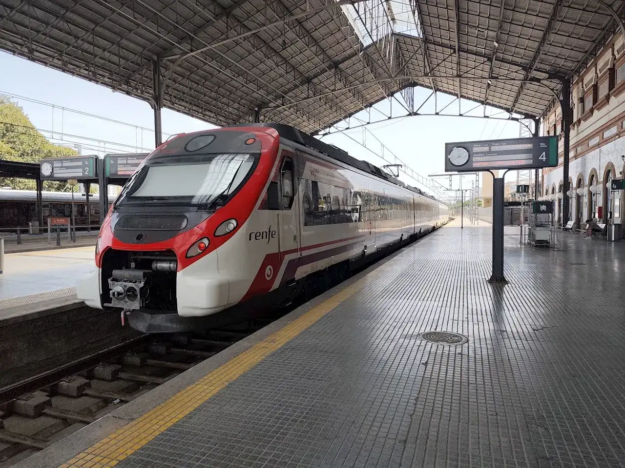 Ett modernt tåg i Spanien, med Renfe-logotypen, står på en solig perrong under ett stort tak.