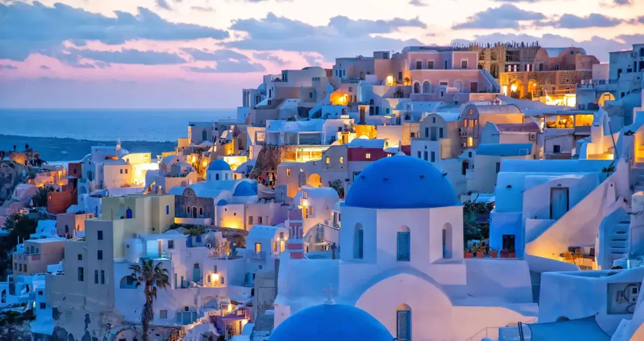 Oia, Santorini: weiße Häuser mit blauen Kuppeln schmiegen sich an den Hang, beleuchtet vom Abendlicht.