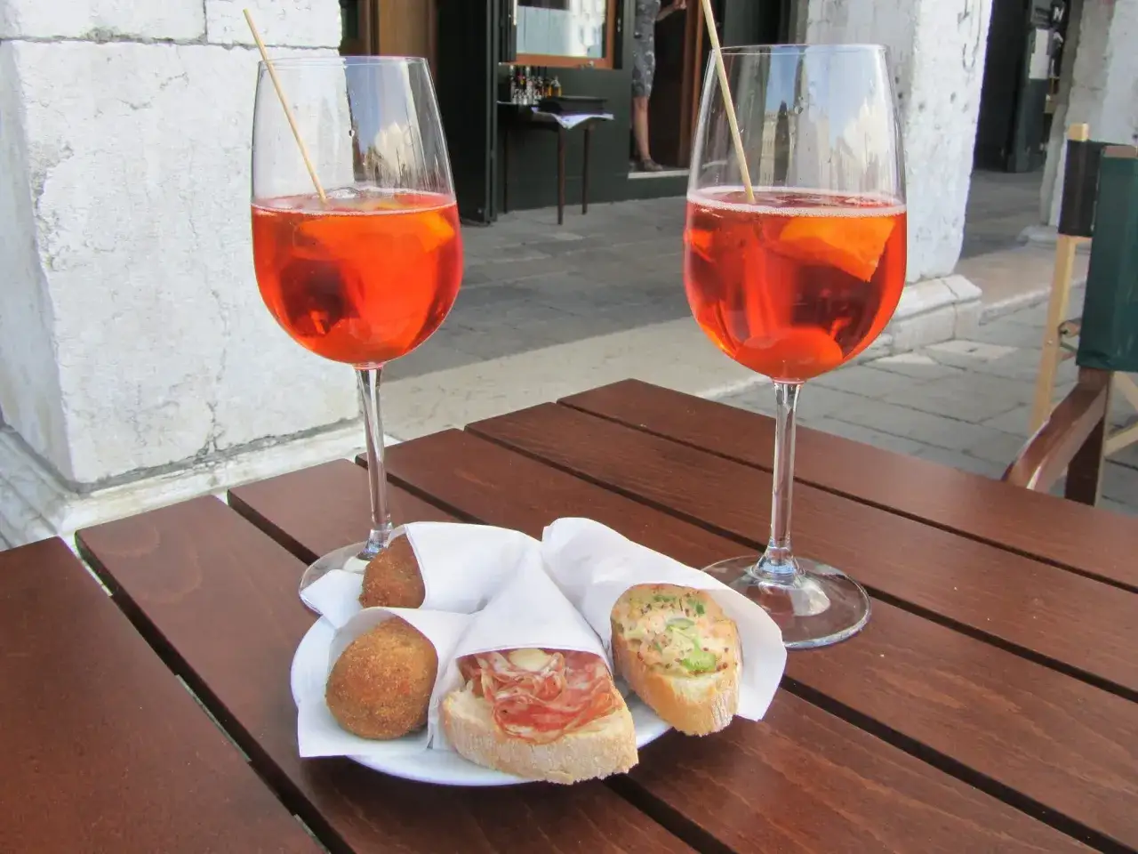 Due calici di Aperol Spritz e stuzzichini su un tavolo di legno, perfetti per un aperitivo in compagnia.