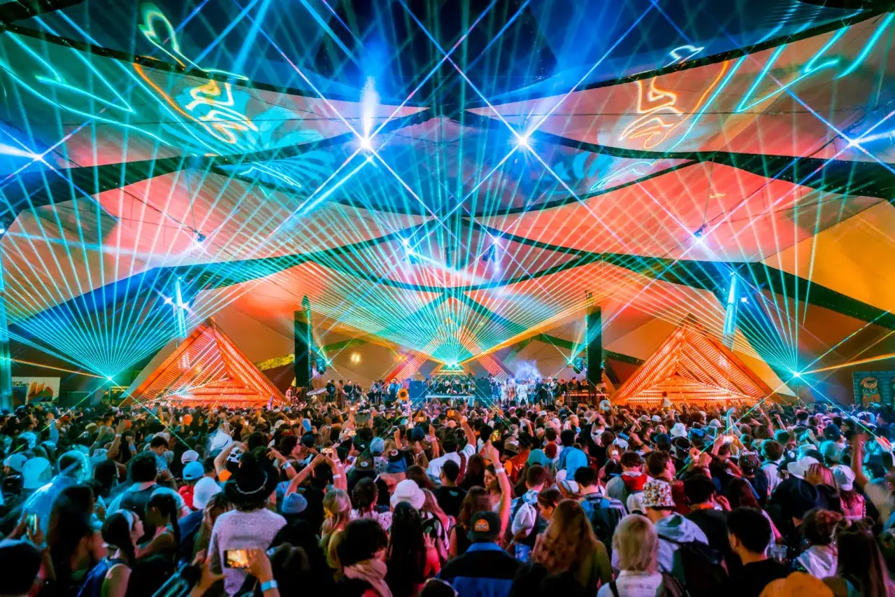 Tłum ludzi w **trance** pod laserami i świetlnymi instalacjami na festiwalu.