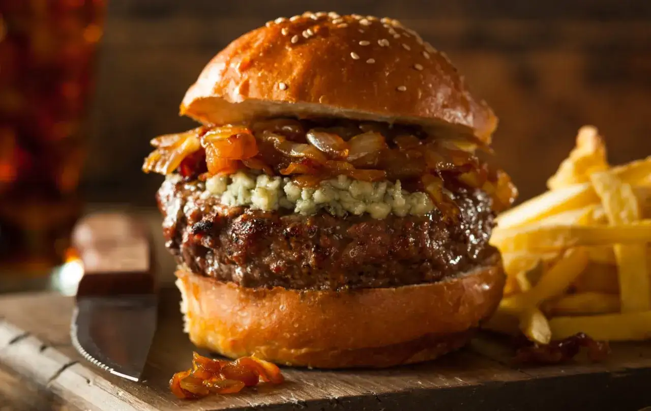Jugosa hamburguesa con queso de cabra desmoronado, cebolla caramelizada y papas fritas crujientes.