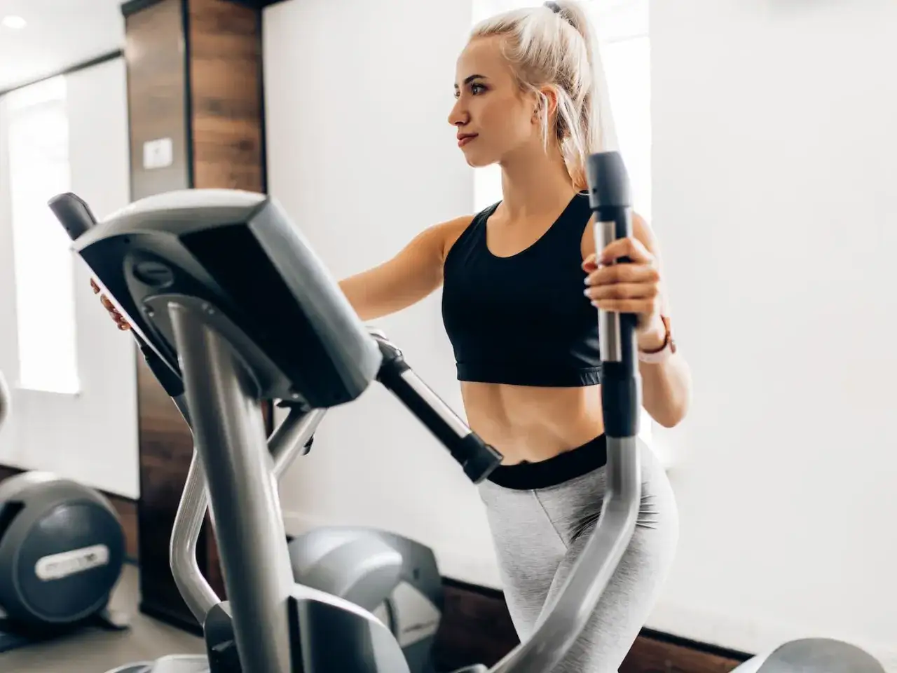 Junge Frau trainiert auf Crosstrainer, um ihren Kalorienverbrauch zu steigern.