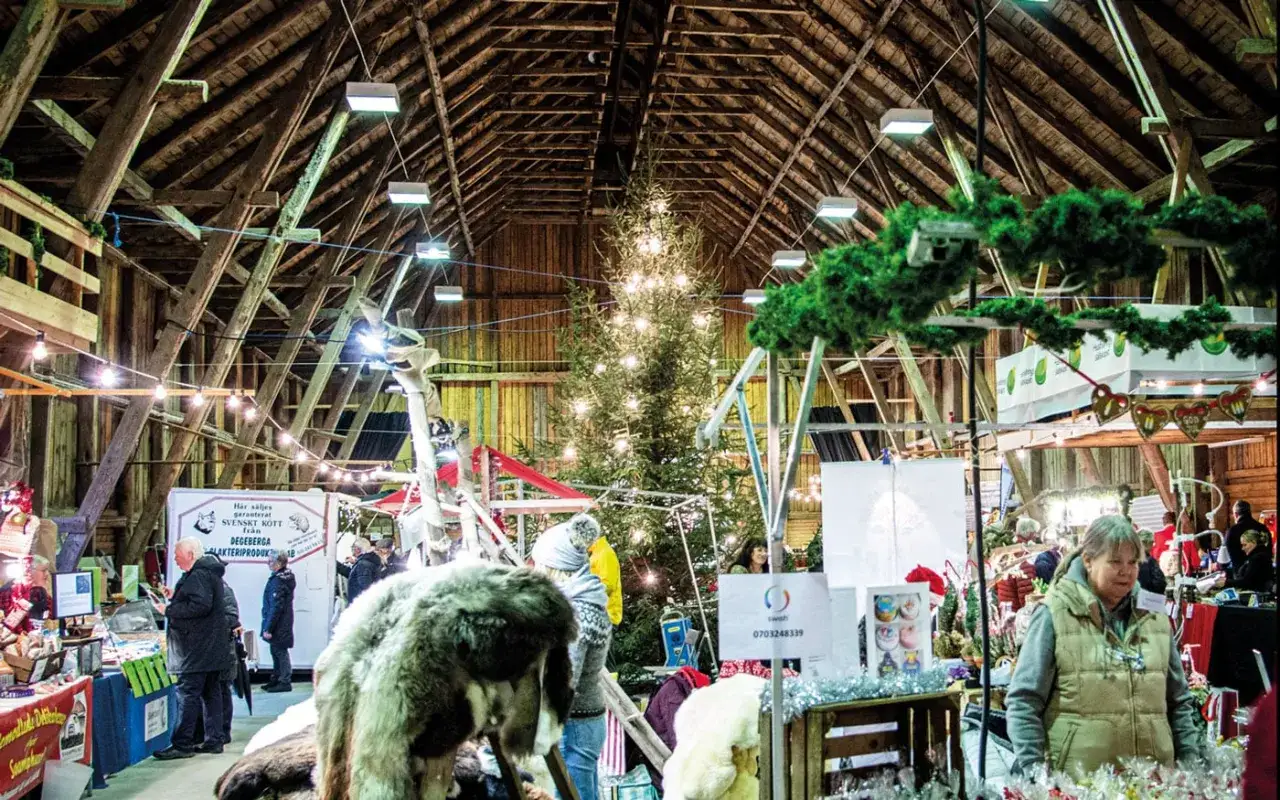 Mysig julmarknad i en lada med julgran och folk som handlar. En härlig stämning som påminner om julmarknader i Skåne.