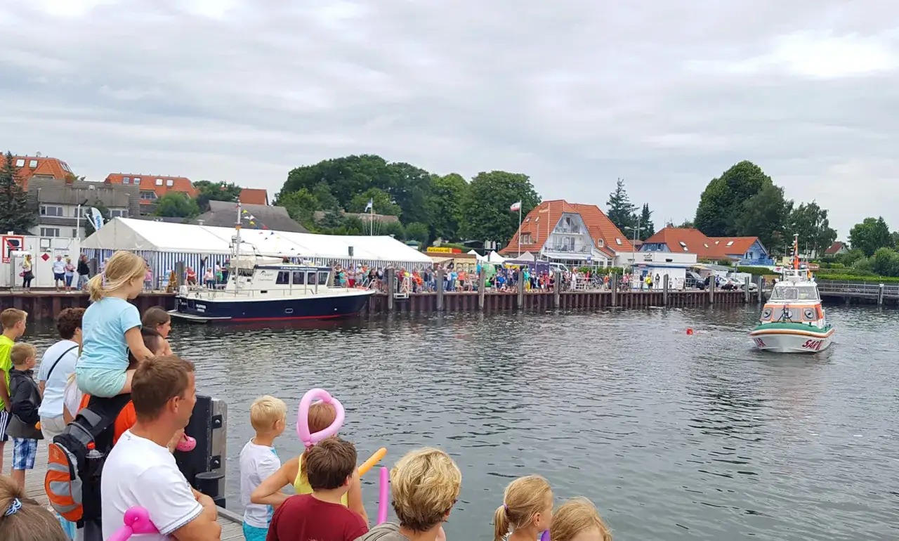 Menschen genießen das bunte Treiben beim Rock am Hafen. Boote liegen im Wasser, eine Rettungsboot fährt vorbei.