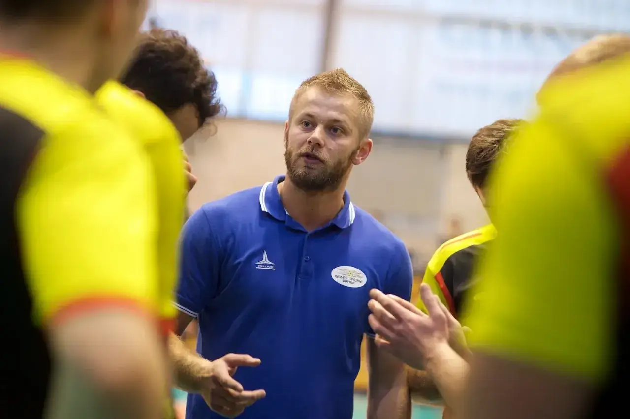 Marcin Markuszewski, trener, w niebieskiej koszulce polo, przemawia do drużyny w żółtych strojach.