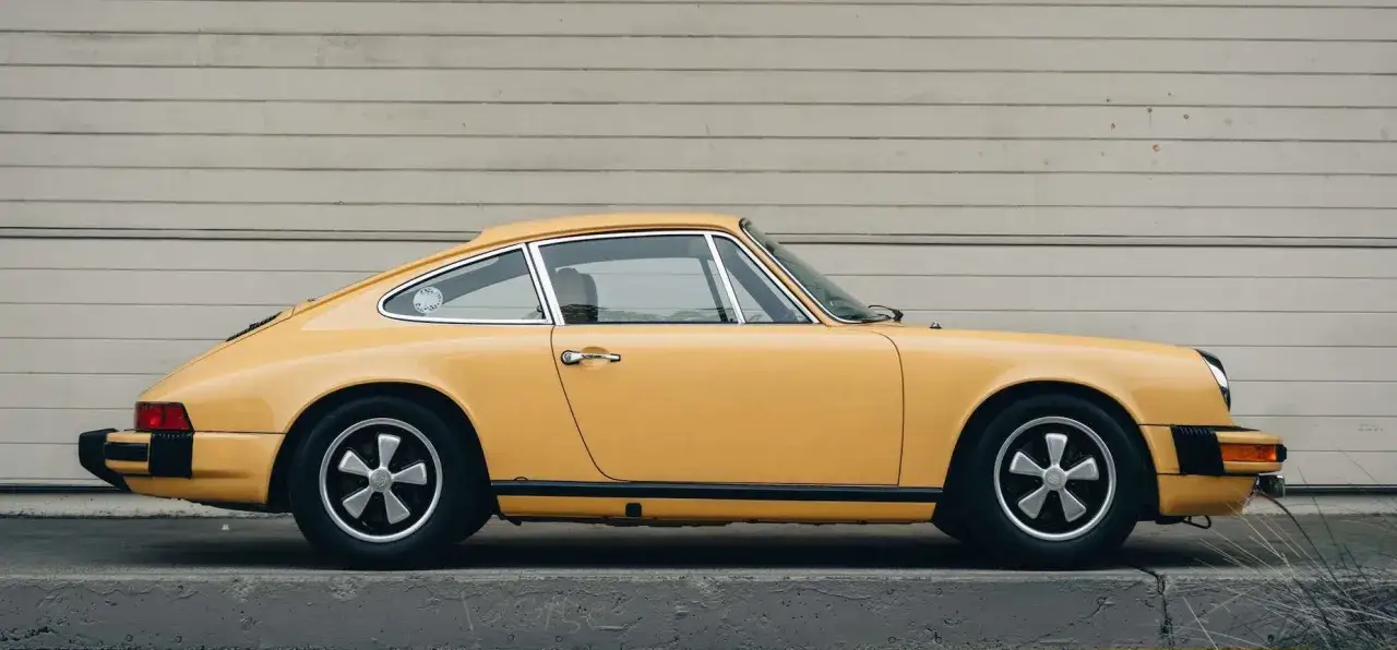 Gelber Porsche 911 G-Modell, klassische Silhouette, steht vor einer Holzwand.