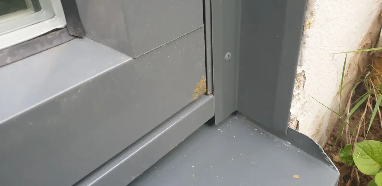 Grå plåt runt ett fönster med en liten fläck av gulaktigt, lågexpanderande fogskum synligt i hörnet.