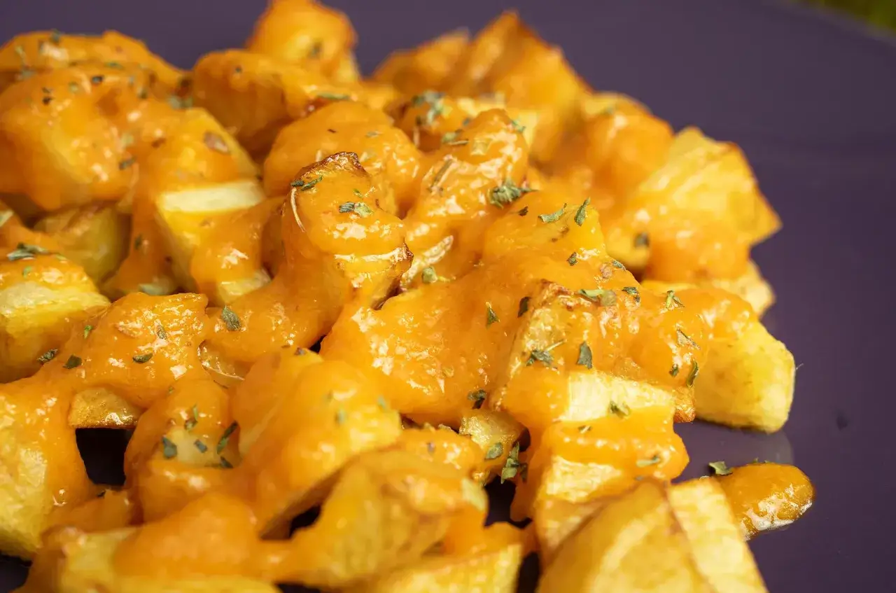 Patatas bravas receta: patatas fritas crujientes cubiertas con una salsa brava cremosa y picante, espolvoreadas con hierbas.