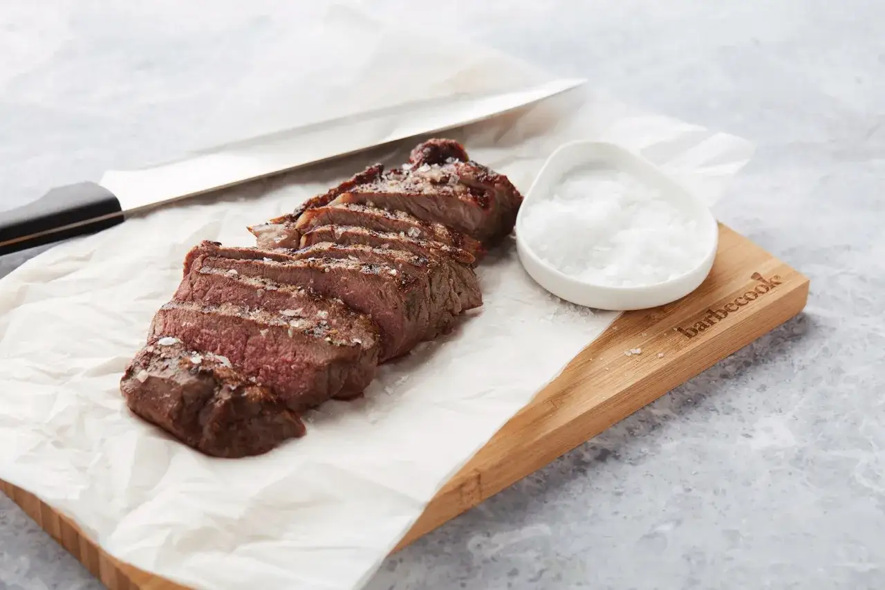 Tranché et saupoudré de gros sel, ce beau morceau de bœuf bleu blanc belge attend d'être dégusté. Un couteau de chef est posé à côté.