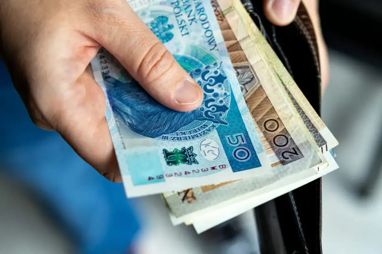 Dłoń trzyma polskie banknoty, w tym 50 i 200 zł. Pieniądze mogą posłużyć na dodatek mieszkaniowy.