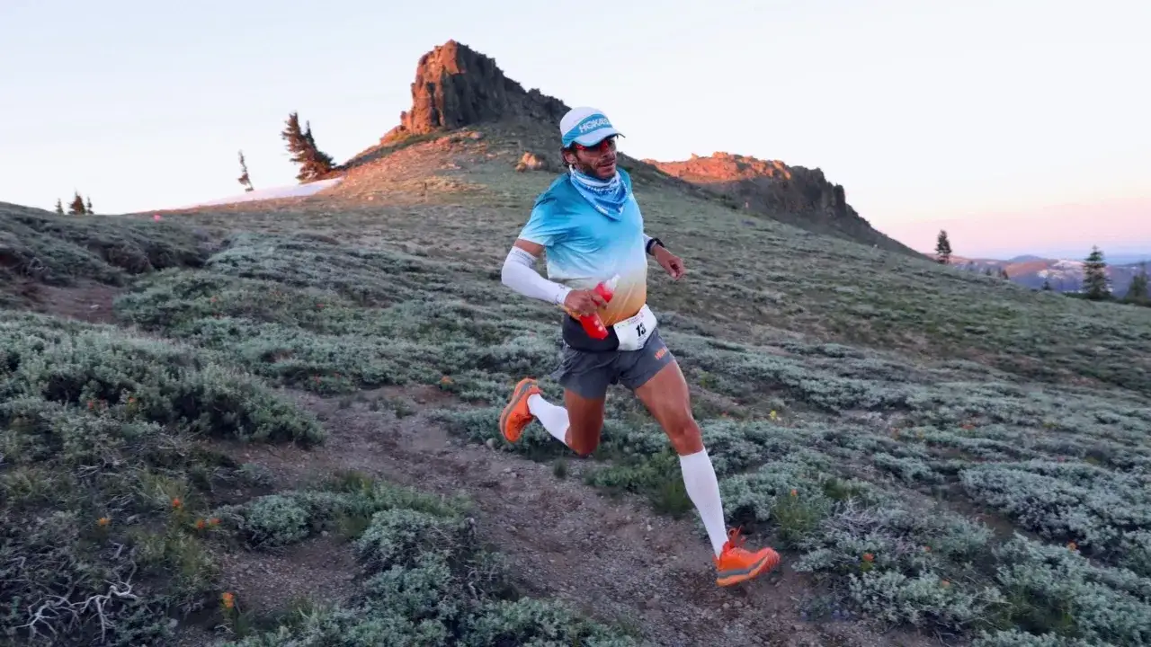 Biegacz w górskim terenie, przygotowujący się do treningu ultramaraton 50 km. Słońce zachodzi za skalistym szczytem.