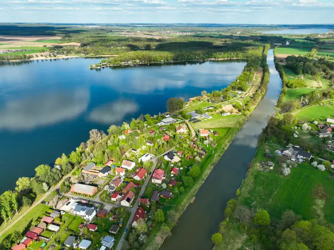 Pławniowice jezioro otoczone zielenią i domkami letniskowymi, z kanałem wodnym biegnącym wzdłuż brzegu.
