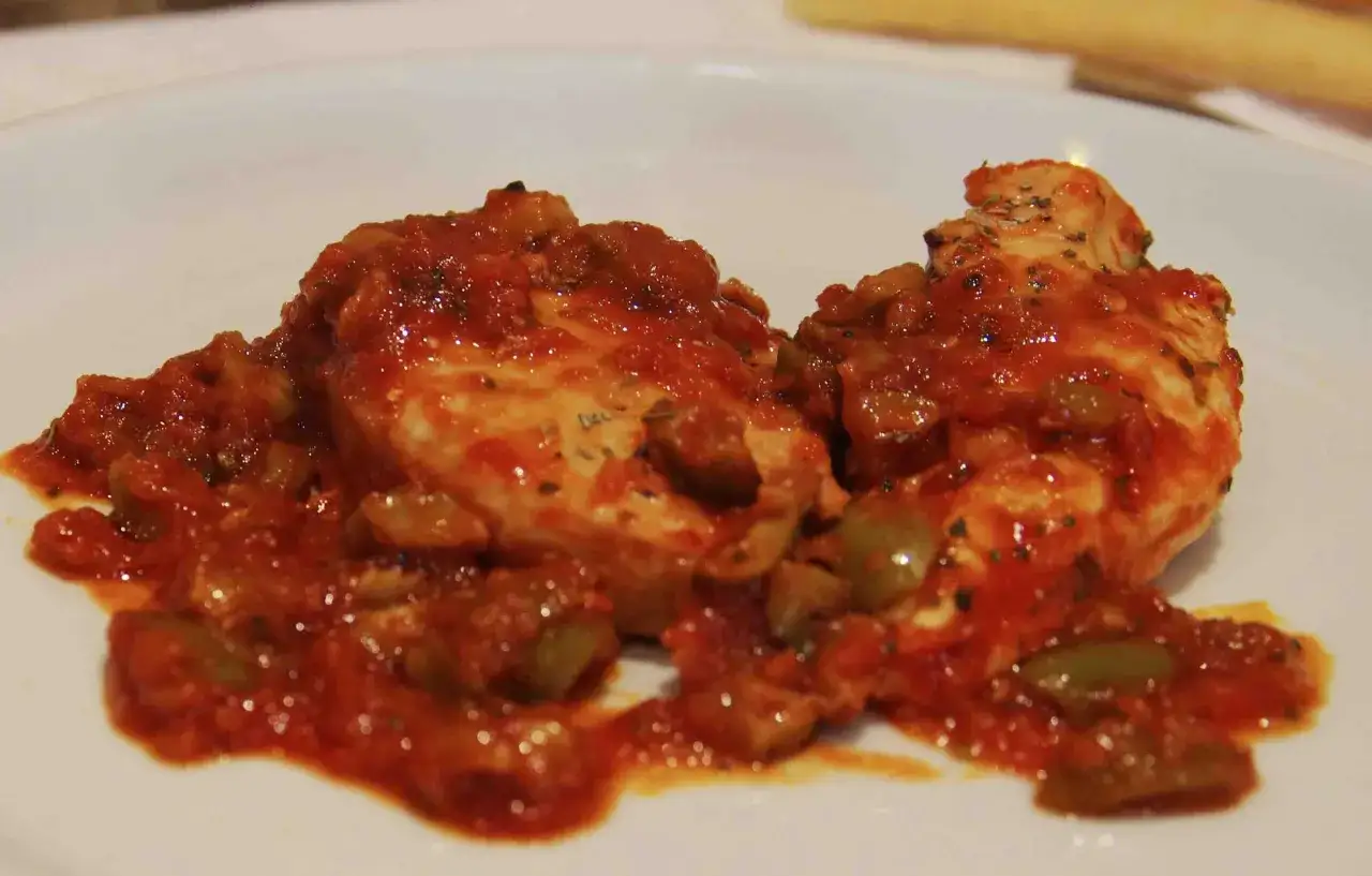 Deux morceaux de poulet nappés d'une sauce tomate savoureuse avec des olives vertes. Un plat simple et appétissant.