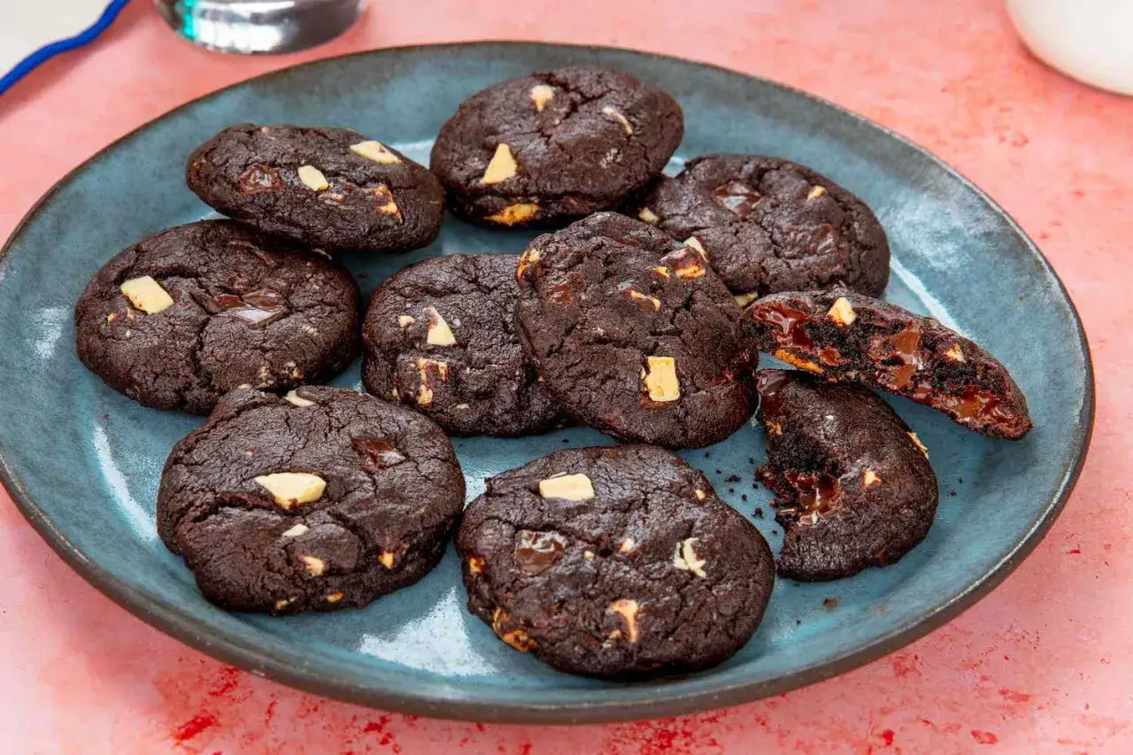 Assiette de biscuits au chocolat noir, parsemés de morceaux de chocolat qui ne fond pas, avec un biscuit cassé révélant un cœur coulant.
