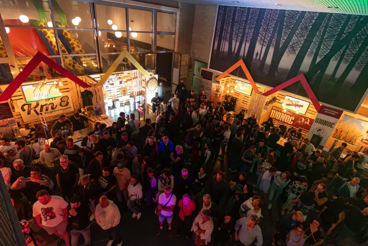 Folla animata in un beer festival, con stand in legno, fusti di birra e persone che socializzano.