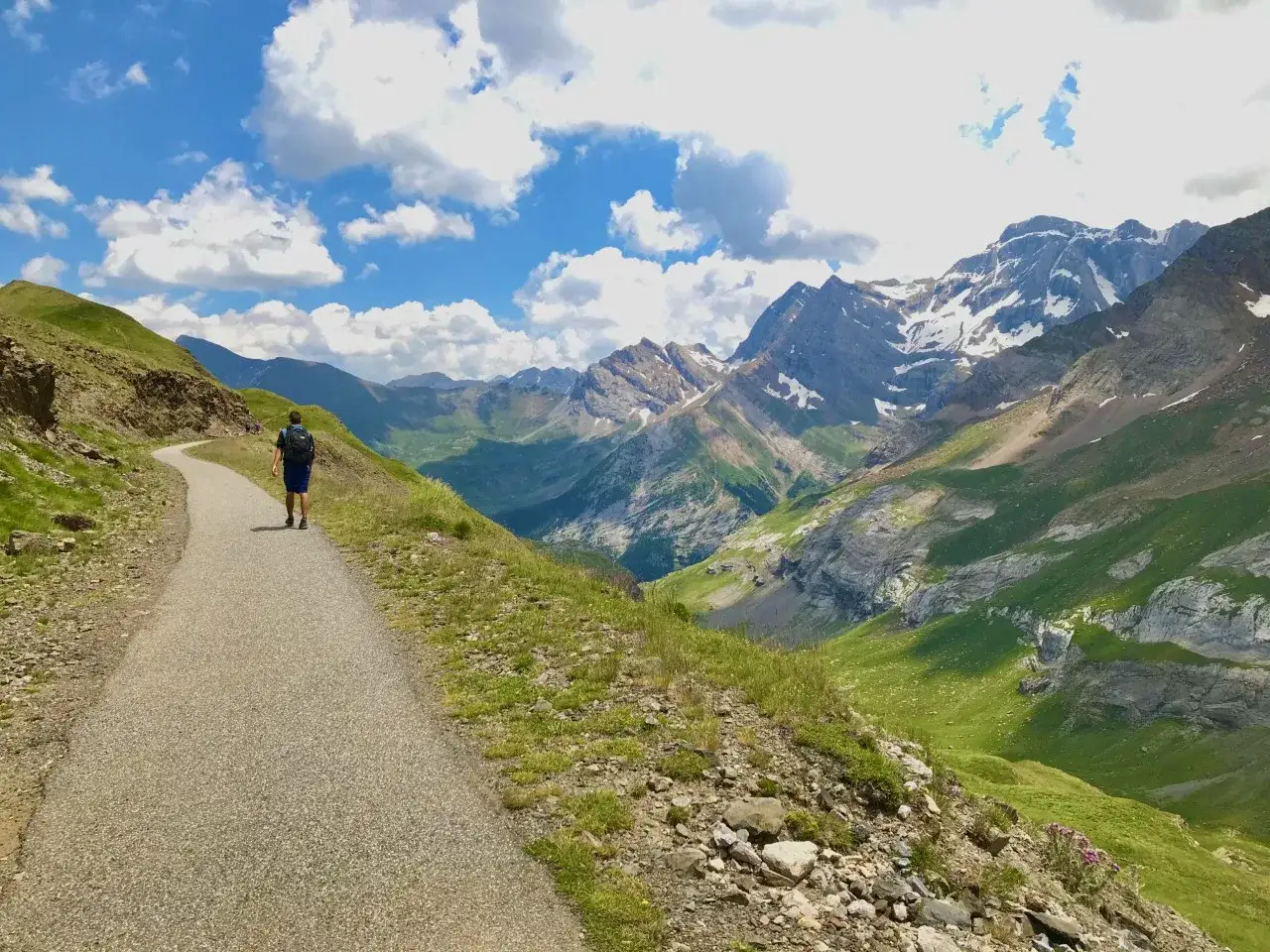 Un randonneur solitaire emprunte un sentier sinueux menant vers le col de tentes, dominant une vallée verdoyante et des montagnes majestueuses.