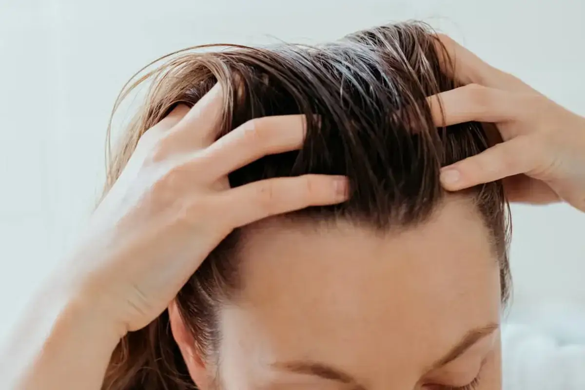 Delikatne dłonie masują skórę głowy, pobudzając wzrost włosów. Widać drobne, **baby hair** przy linii czoła, zapowiadające gęstsze włosy.