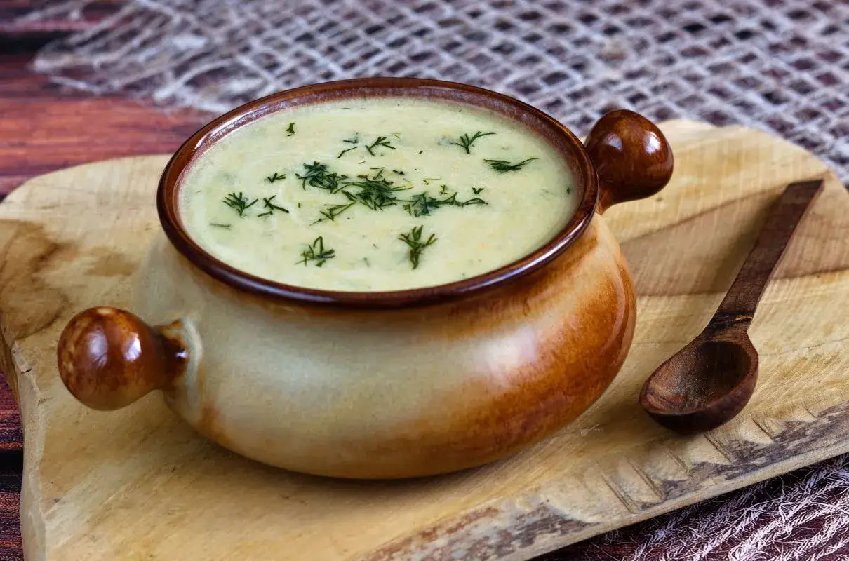 Aksamitna zupa z boczkiem, udekorowana koperkiem, w glinianej miseczce z drewnianą łyżką na desce.