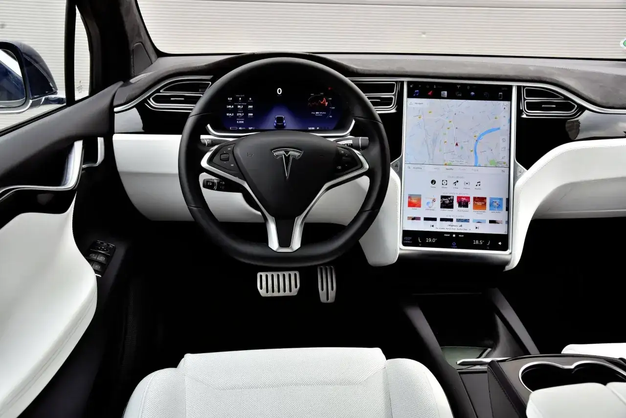 Wnętrze Tesli Model X z białymi skórzanymi fotelami, dużym ekranem dotykowym i cyfrowym kokpitem.