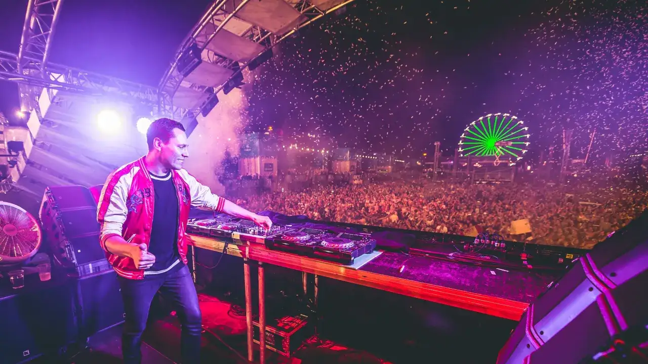 DJ Tiesto gra dla tłumu w Polsce, sypią się konfetti, a w tle widać diabelski młyn.
